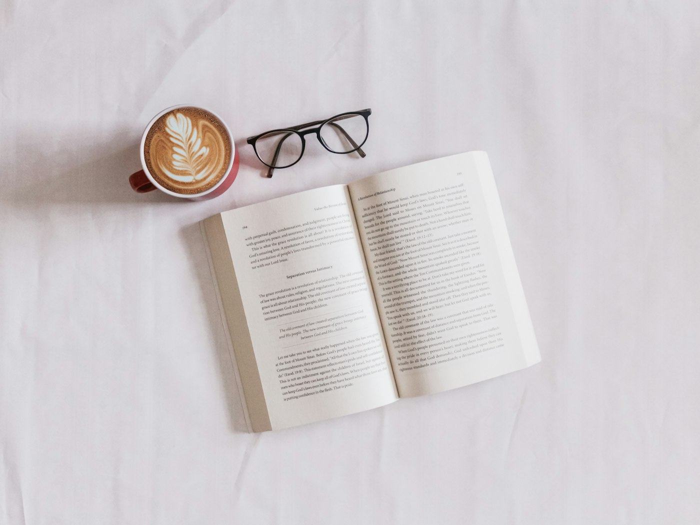 Un libro aperto accanto a una tazza di cappuccino e a un paio di occhiali